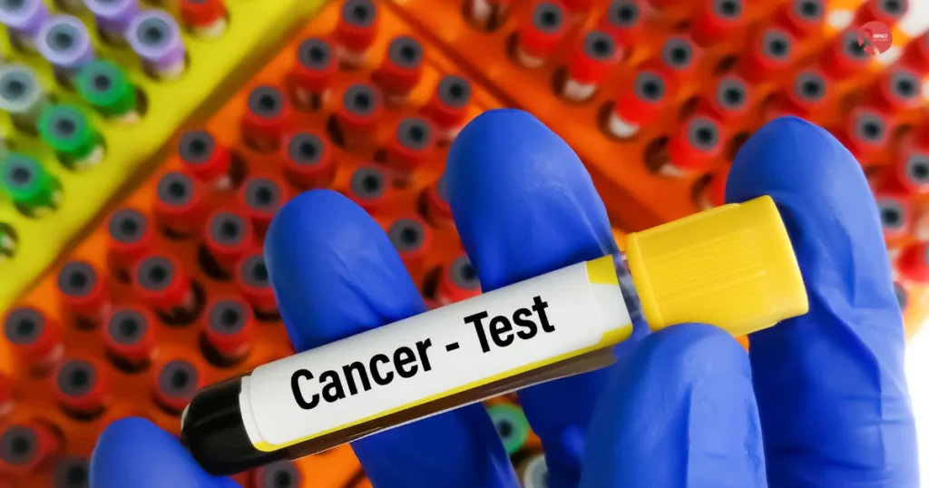 Close-up of a lab technician’s gloved hand holding a blood sample labeled “Cancer Test” with colorful test tubes in the background