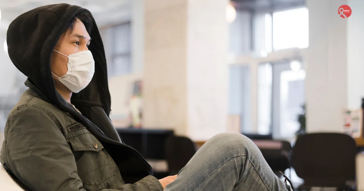 Person wearing a face mask sitting in a hospital waiting area while traveling for cancer treatment