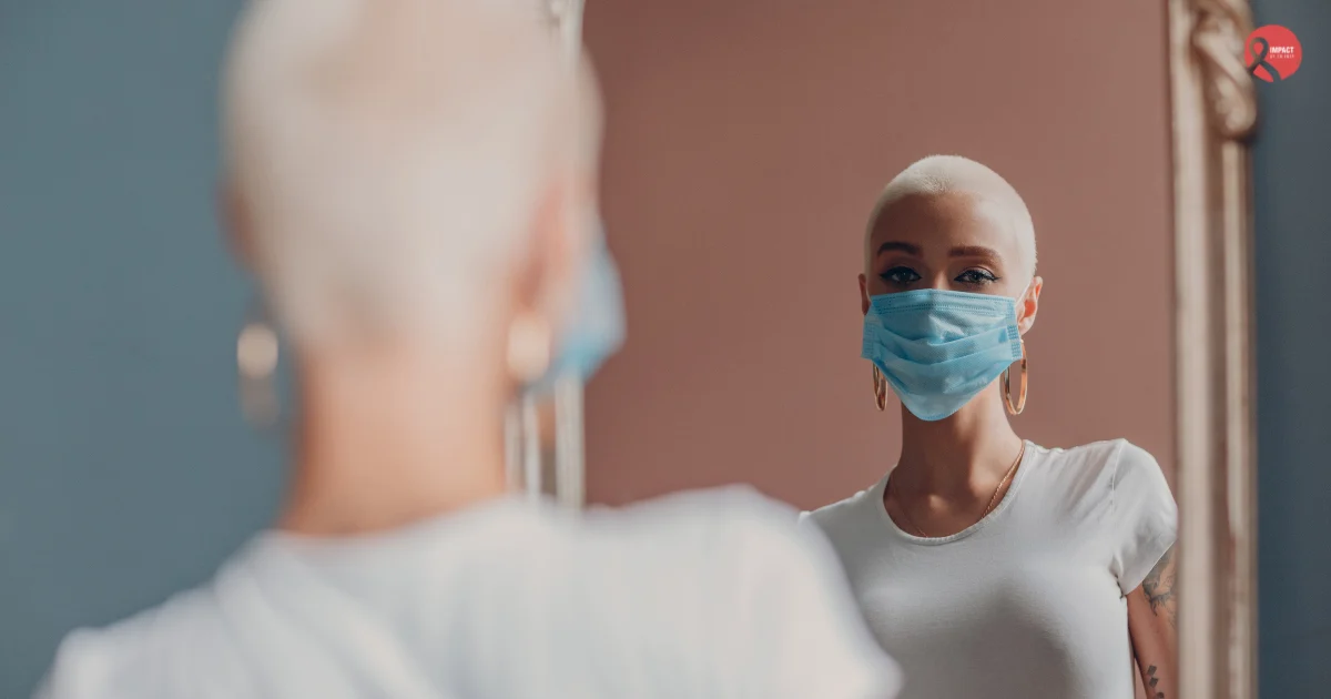 A woman with a shaved head wearing a mask looks at her reflection in the mirror, symbolizing strength and awareness as common cancer myths are busted.